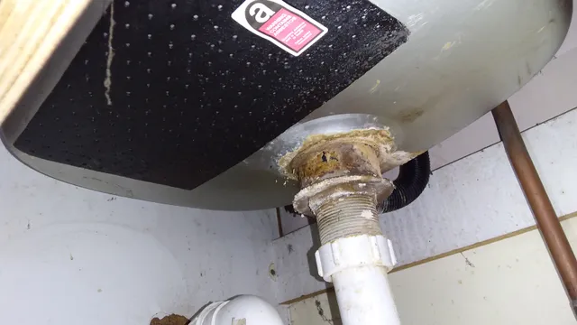 Asbestos-containing sink pad fixed to the underside of a stainless-steel sink. The black bitumen-based pad was commonly used for sound insulation and condensation control.