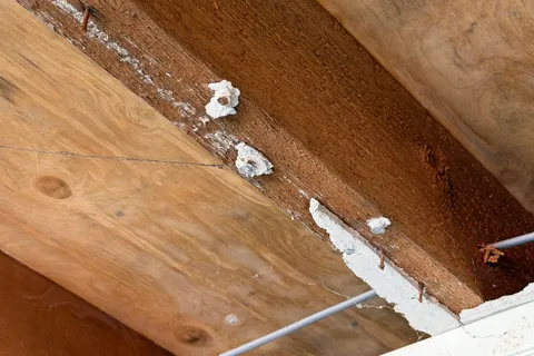 Damaged asbestos insulating board with visible debris around ceiling fixings in the garage. The material tested positive for asbestos and was in poor condition.