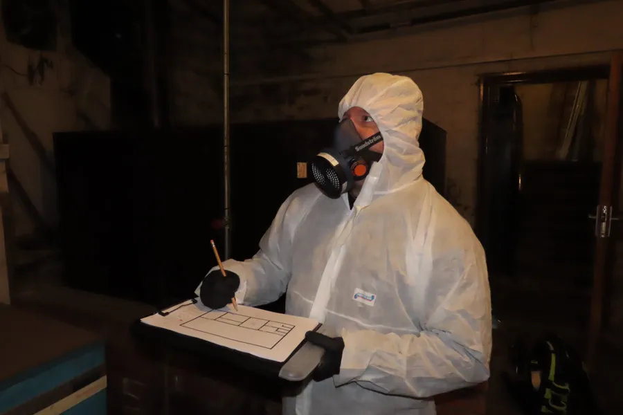 A qualified asbestos surveyor wearing protective coveralls, gloves and respiratory equipment records findings during an asbestos inspection at a commercial property in Yorkshire.