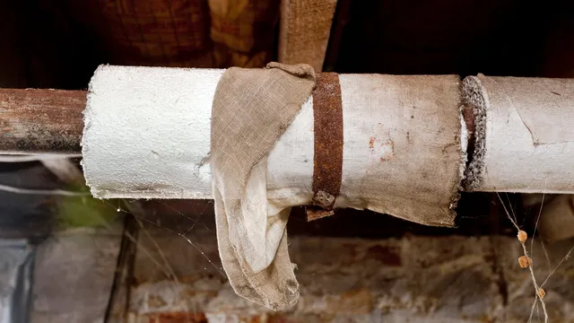 Damaged asbestos-containing paper insulation wrapped around older pipework. The torn covering exposes the underlying material, increasing the risk of fibre release if disturbed.