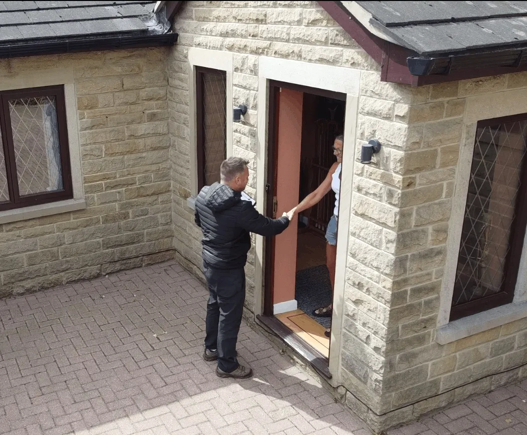 Surveyor greeting a homeowner at the front door of a stone-built house before starting a homebuyer asbestos survey
