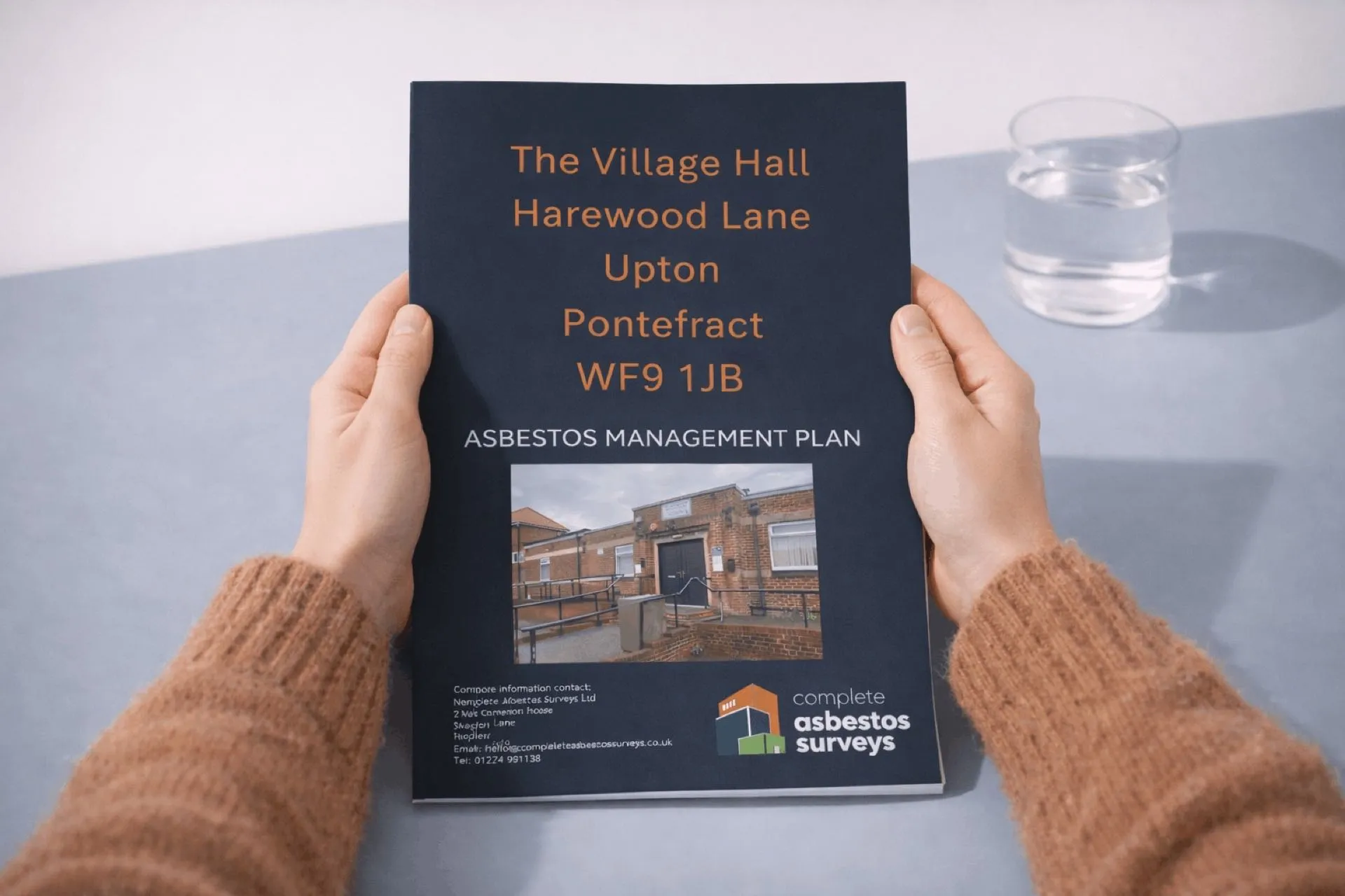 Hands holding a printed Complete Asbestos Surveys asbestos management plan for a village hall