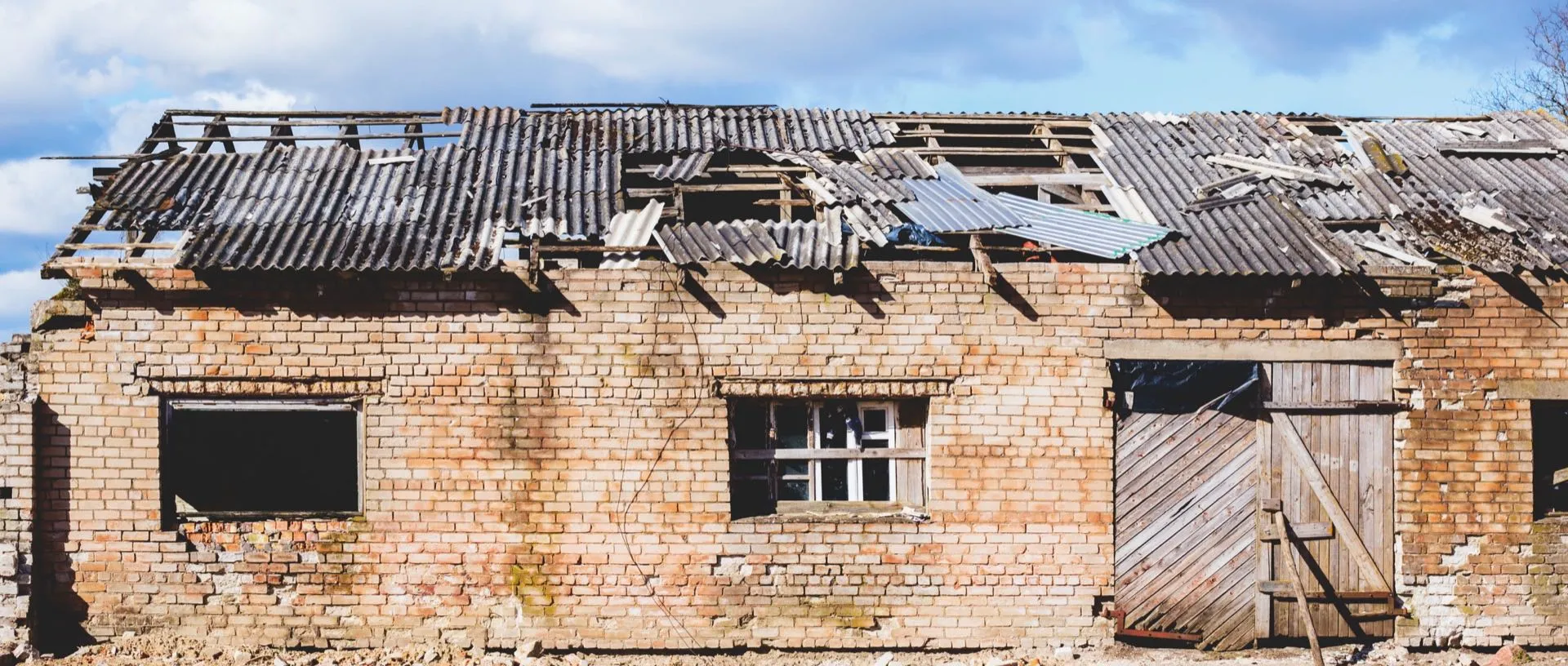 Derelict brick building with a damaged corrugated asbestos cement roof awaiting removal