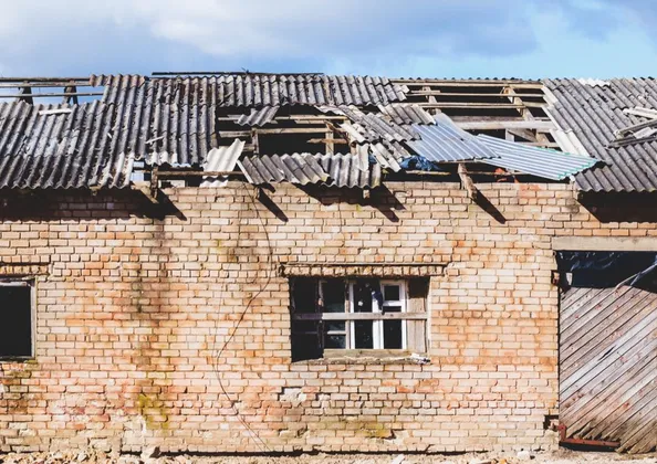 Derelict brick building with a damaged corrugated asbestos cement roof awaiting removal