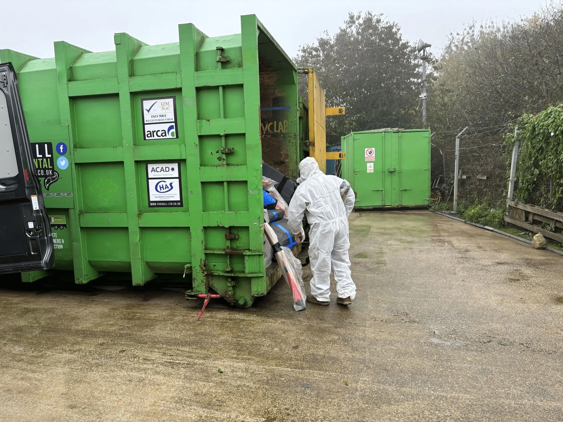 Operative in protective coveralls loading wrapped and sealed asbestos waste into a licensed disposal container