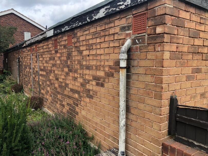 Asbestos cement rainwater down pipe on rear of external garage