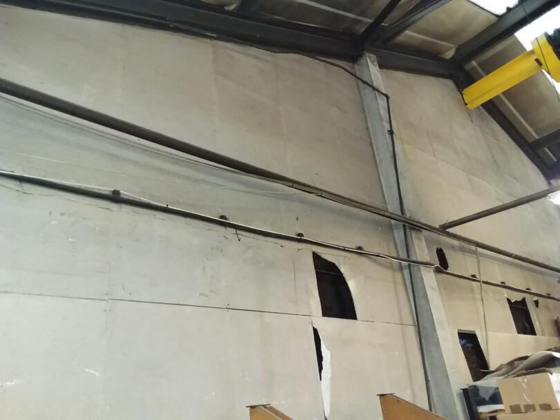 Damaged asbestos insulating board panels on gable ends within production factory
