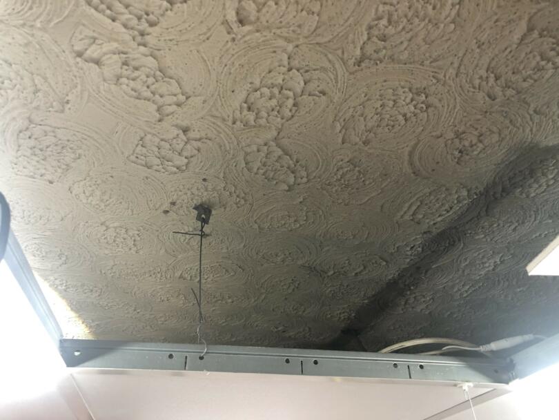 Thick asbestos textured coating ceiling above suspended ceiling tiles in commercial shop