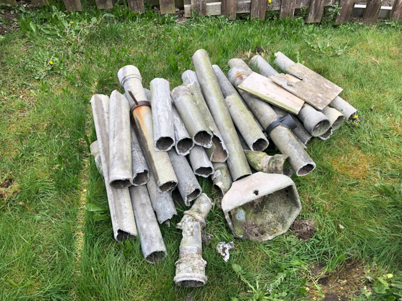 Pile of asbestos cement rainwater pipes in front garden of domestic property